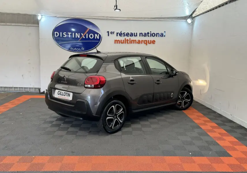 Vue 3/4 arrière droite d'une Citroën C3 gris foncé avec protections latérales noires et jantes bicolores dans un showroom.