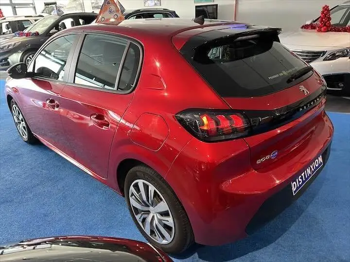 Vue 3/4 arrière droite d'une Peugeot 208 rouge Elixir Metal avec feux arrière allumés en concession.