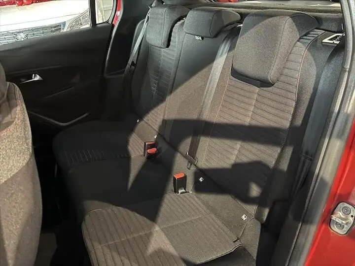 Vue intérieure arrière montrant les sièges arrière noirs d'une Peugeot 208 rouge Elixir Metal, avec ceinture de sécurité visible.