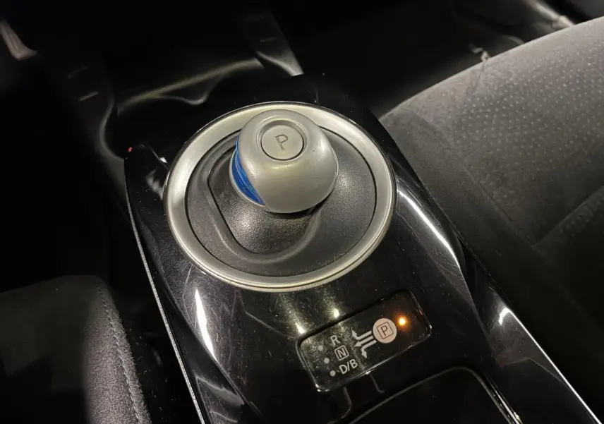 Gros plan sur le levier de vitesses automatique rond et noir avec bouton "P" dans l'habitacle sombre d'une Nissan Leaf rouge 2017.