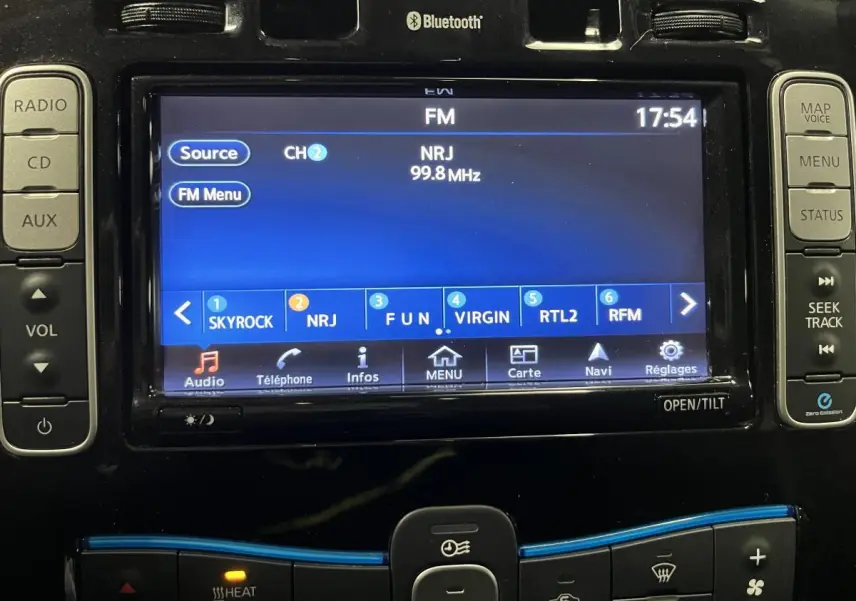 Gros plan sur l'écran tactile central et commandes audio d'une Nissan Leaf rouge de 2017, affichant la radio FM NRJ.