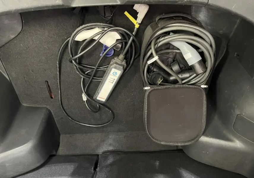 Gros plan sur le coffre d'une Nissan Leaf rouge 2017, montrant les câbles de recharge électrique rangés.