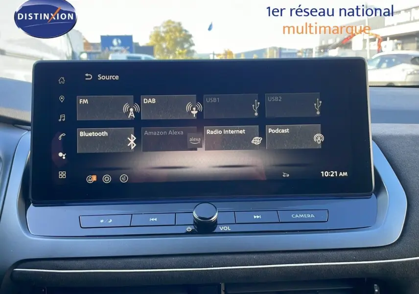 Écran tactile central du Nissan Qashqai blanc nacré avec toit noir, affichant les sources audio et commandes multimédia.