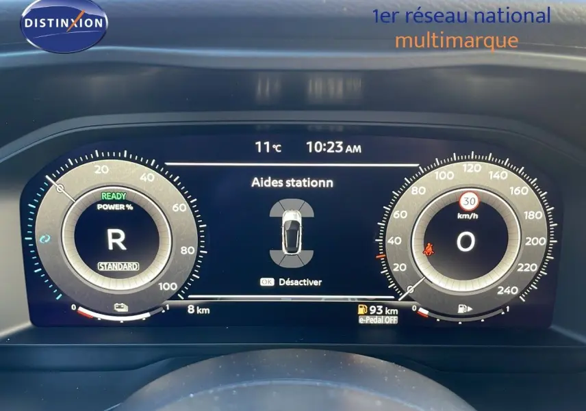 Tableau de bord numérique du Nissan Qashqai blanc nacré, affichant l'aide au stationnement et la vitesse à 0 km/h.