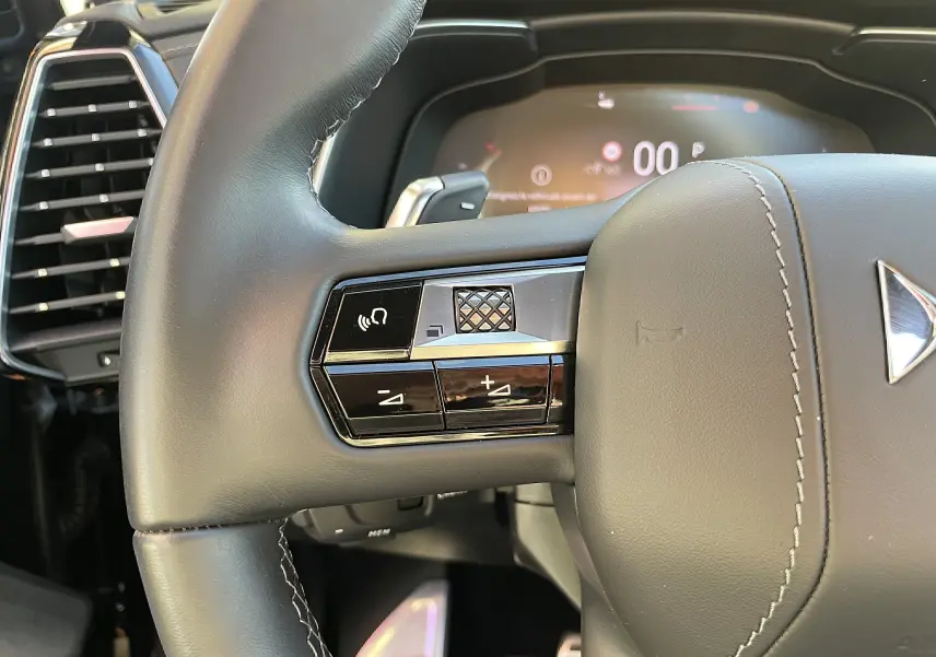 Gros plan sur le volant cuir noir du DS7 2024 avec commandes intégrées et tableau de bord numérique en arrière-plan.