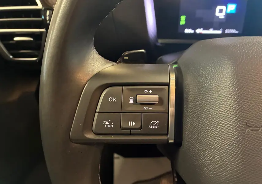 Gros plan sur les commandes à gauche du volant noir du Citroën C4 X 2024, avec affichage numérique en arrière-plan.