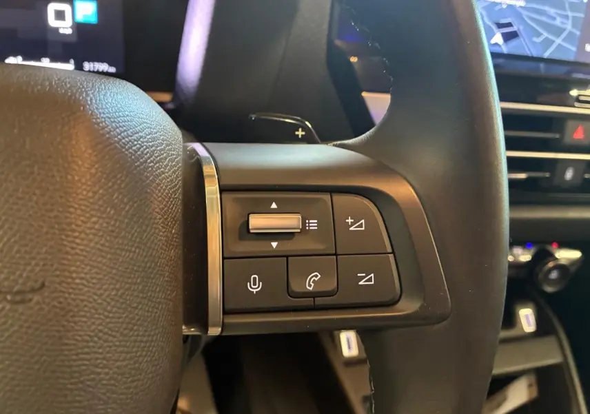 Gros plan sur les commandes au volant côté gauche du Citroën C4 X gris 2024, avec tableau de bord et écran GPS en arrière-plan.