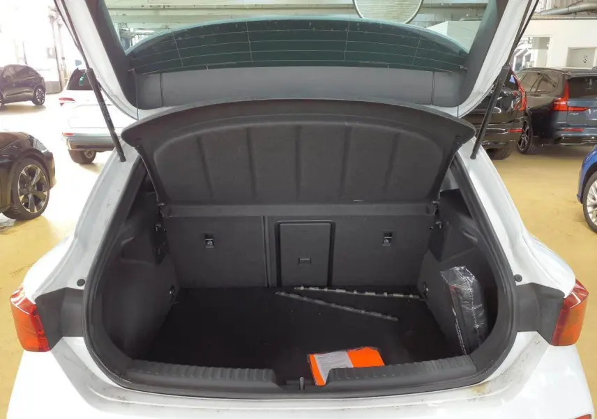 Coffre ouvert vu de l'arrière d'une CUPRA Leon blanc Nevada, montrant l'espace de chargement vide avec quelques objets.