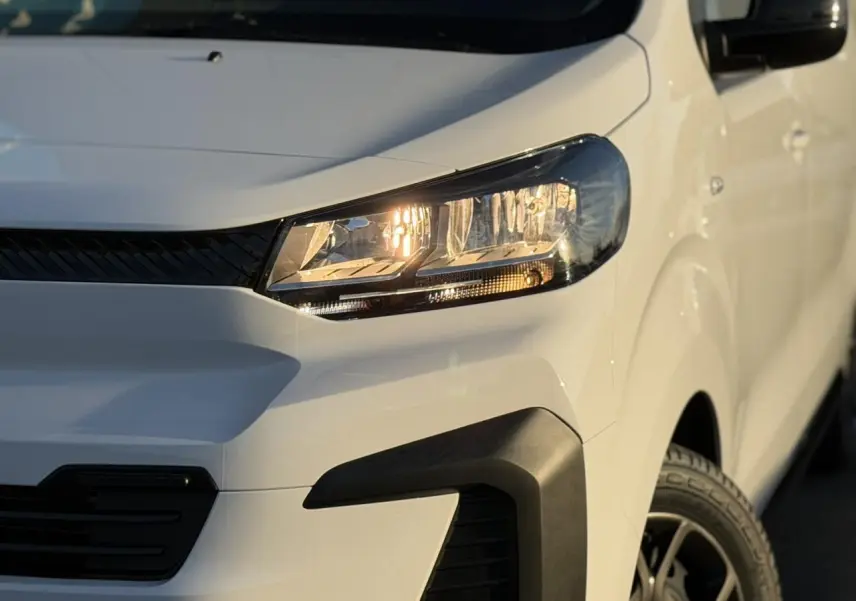Gros plan sur l'avant droit du Citroën Jumpy XL blanc Icy avec phares allumés et bouclier noir du Pack Look.