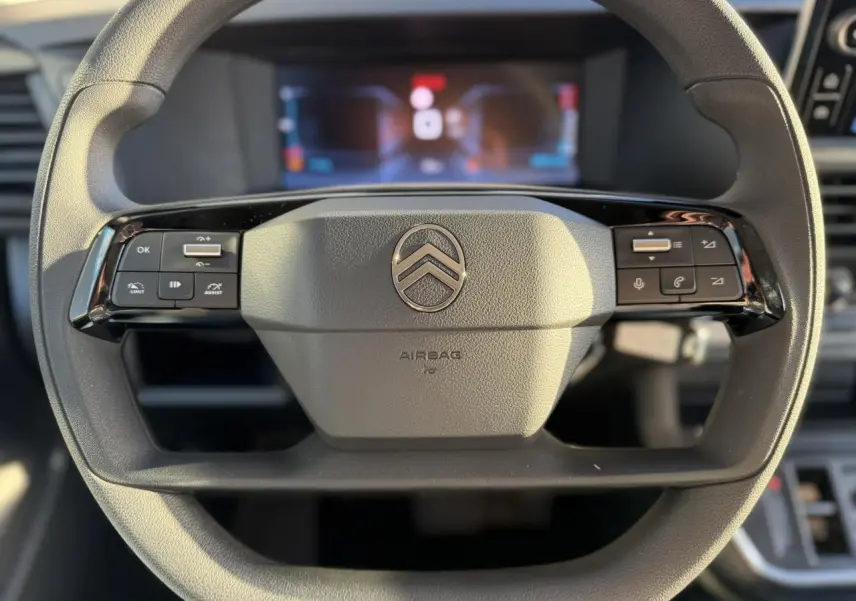 Gros plan sur le volant multifonction noir du Citroën Jumpy XL 2025 avec tableau de bord numérique en arrière-plan flou.