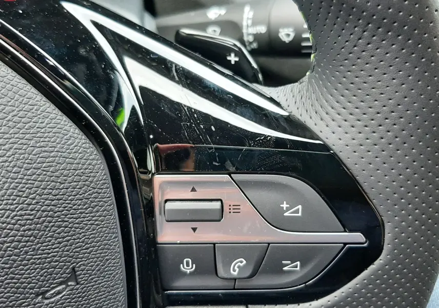 Gros plan sur les commandes gauche du volant perforé noir de la Peugeot 308 Bleu Lagoa 2025 hybride.