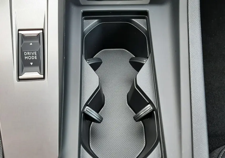 Gros plan sur la console centrale noire de la Peugeot 308 1.2 Hybrid 145ch GT avec porte-gobelets et bouton Drive Mode.
