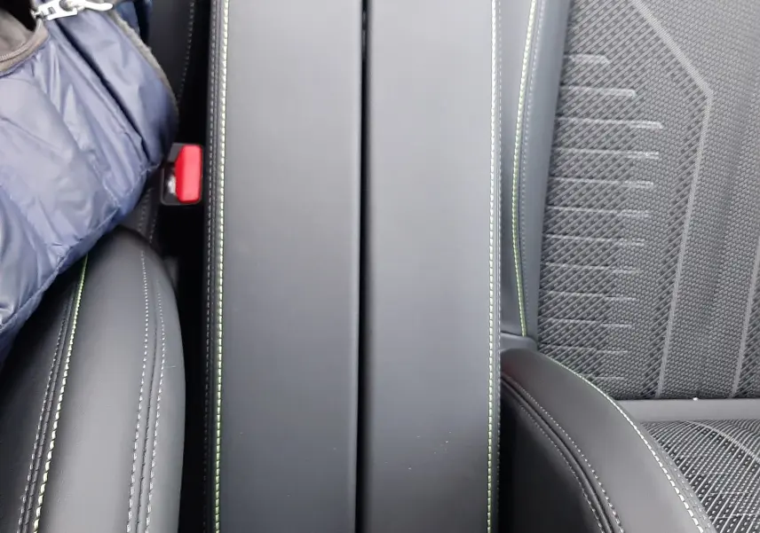 Vue rapprochée de l'accoudoir central noir avec surpiqûres vertes et sièges en tissu gris de la Peugeot 308 Hybrid 2025.
