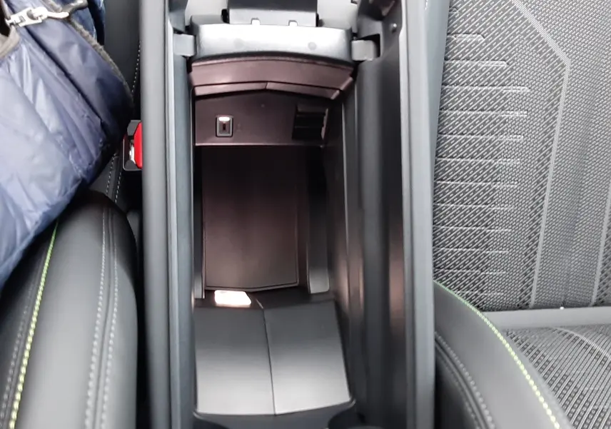 Vue plongeante sur le rangement central ouvert de la Peugeot 308 2025, intérieur noir avec surpiqûres vertes visibles.