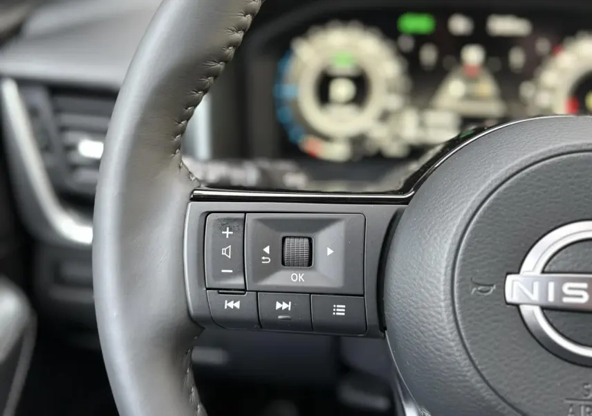 Gros plan sur le volant cuir gris du Nissan Qashqai 2025 avec commandes multifonctions et tableau de bord numérique flou en arrière-plan.