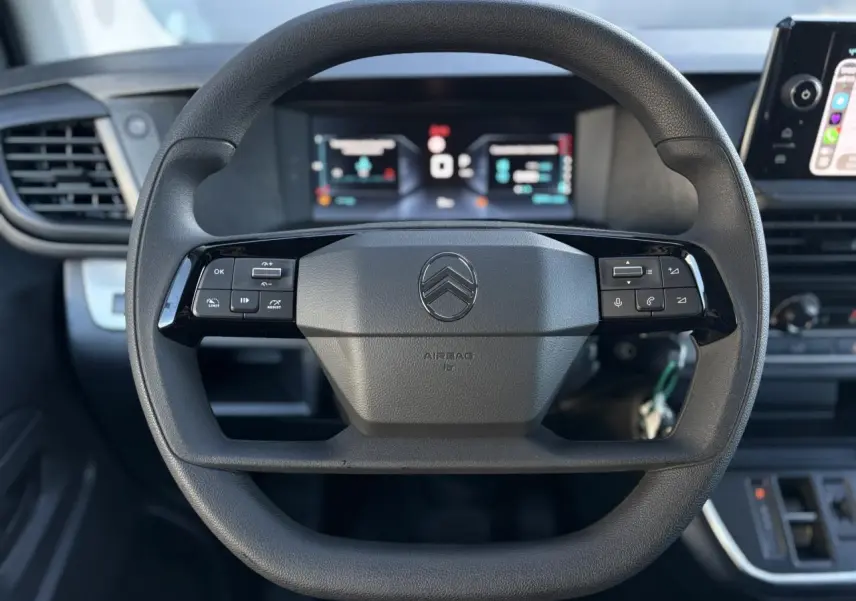 Volant noir Citroën Jumpy XL 2025 avec commandes intégrées, tableau de bord numérique et écran tactile visible en arrière-plan.
