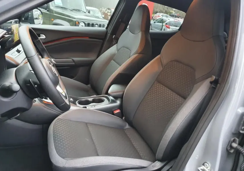 Intérieur du Nissan Juke 2025 en gris céramique, vue côté conducteur sur les sièges avant et console centrale avec porte-gobelets.