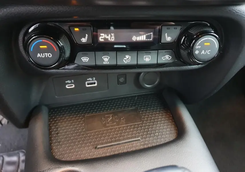 Gros plan sur la console centrale du Nissan Juke 2025, montrant la climatisation automatique et le chargeur sans fil.