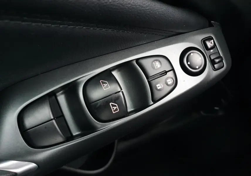 Gros plan sur les commandes de lève-vitres et rétroviseurs côté conducteur du Nissan Juke gris céramique 2025.