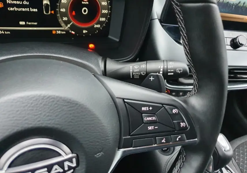 Vue rapprochée du volant noir du Nissan Juke 2025 avec commandes de régulateur et tableau de bord numérique.