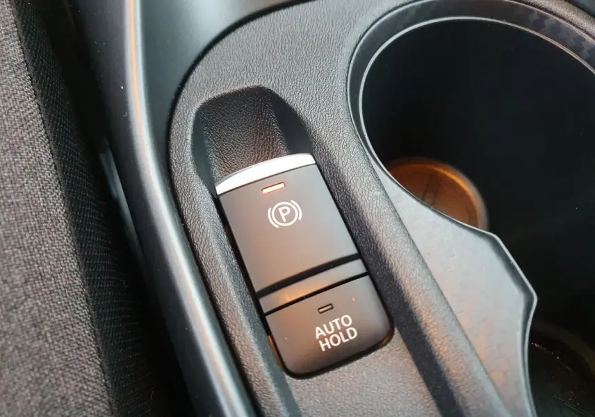 Gros plan sur le frein à main électrique avec fonction Auto Hold et porte-gobelets du Nissan Juke gris céramique 2025.