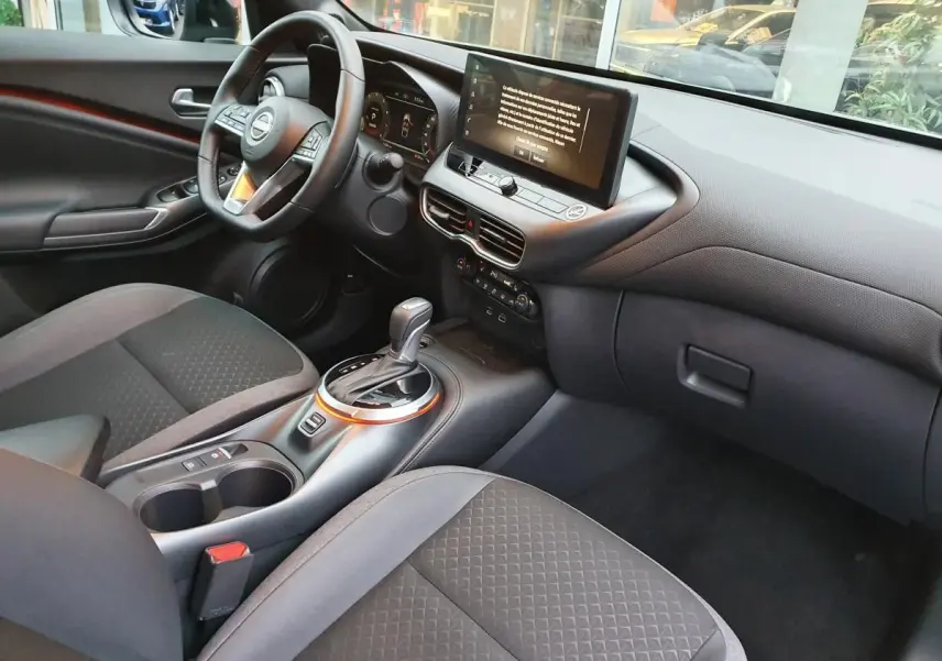 Intérieur du Nissan Juke 2025 en gris céramique, vue côté conducteur sur tableau de bord et console centrale avec écran tactile.