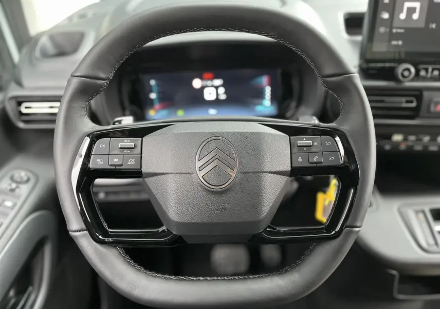 Vue rapprochée du volant cuir multifonctions du Citroën Berlingo Multispace 2025 avec tableau de bord numérique en arrière-plan.