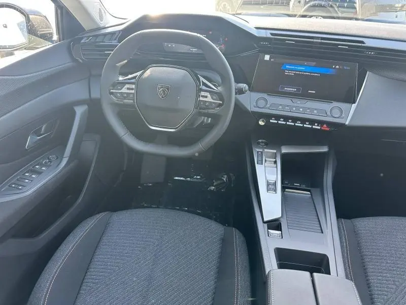 Vue intérieure avant centrée sur le volant multifonction et la console centrale d'une Peugeot 308, sièges tissu gris.