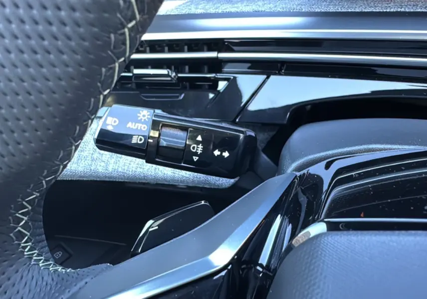 Gros plan sur la manette des feux et clignotants côté gauche du volant cuir du Peugeot 3008 Hybrid blanc toit noir.