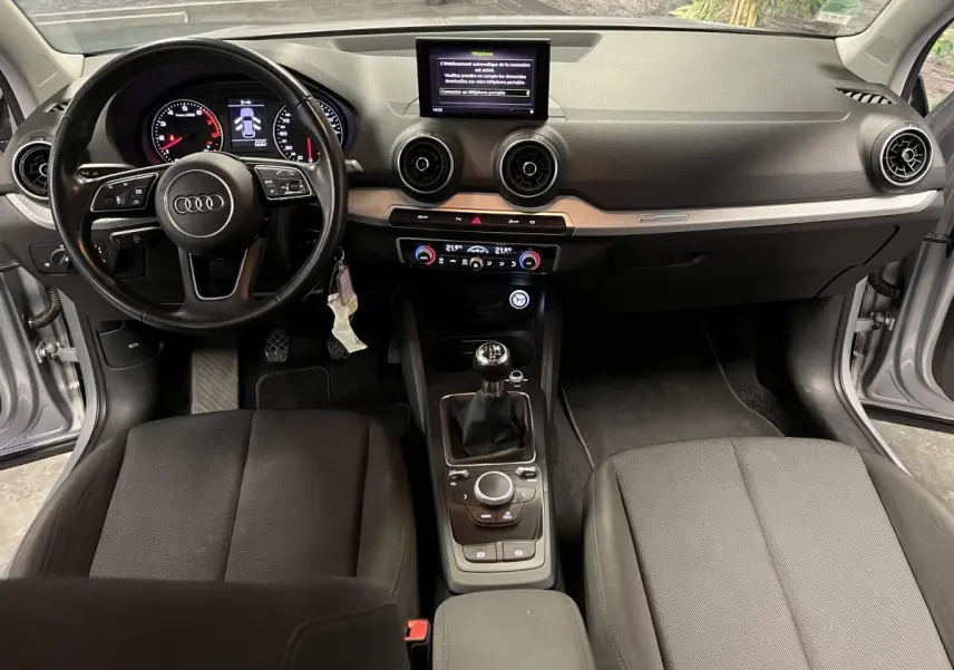 Intérieur Audi Q2 Business line 2019 vu de face, volant cuir, tableau de bord noir et console centrale avec boîte manuelle.