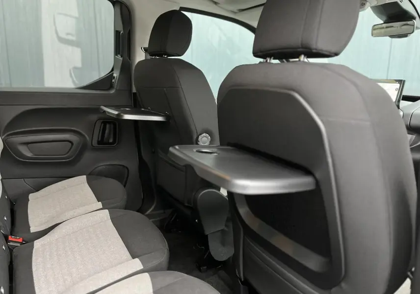 Vue intérieure arrière droite du Citroën Berlingo Multispace 2025 avec sièges gris et tablettes pliantes noires.