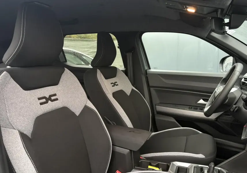 Vue intérieure côté droit montrant les sièges avant gris clair et noir avec logo Duster brodé sur appuie-tête.