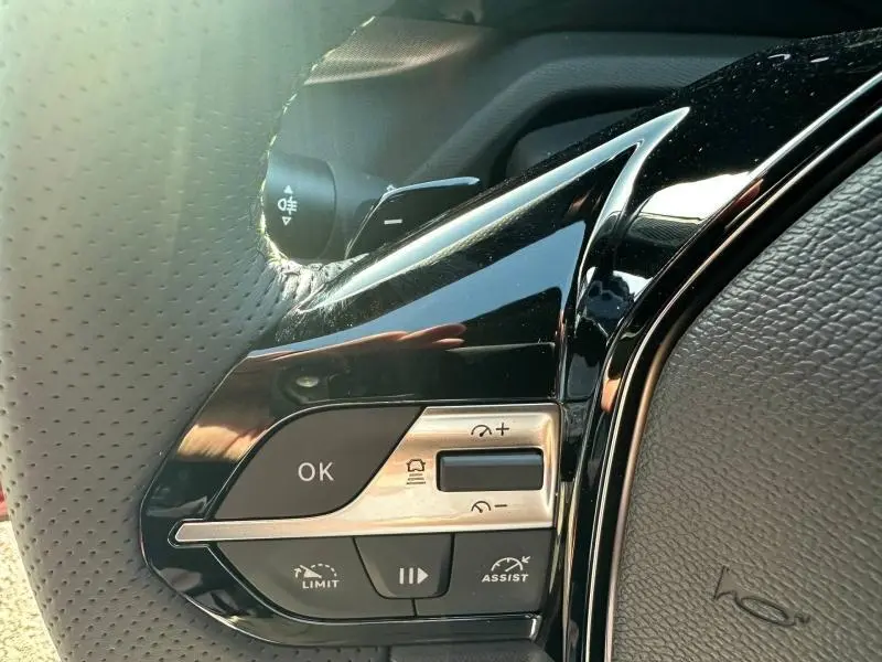 Gros plan sur les commandes multifonctions gauche du volant noir perforé de la Peugeot 308 Rouge Elixir.