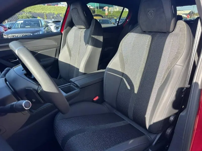 Vue intérieure des sièges avant en tissu et cuir noir de la Peugeot 308 Rouge Elixir, avec accoudoir central et volant multifonction.