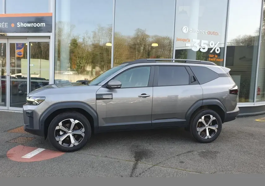 Vue de profil côté gauche d’un Dacia Bigster gris schiste avec jantes alliage 18” diamantées, toit panoramique et barres de toit.