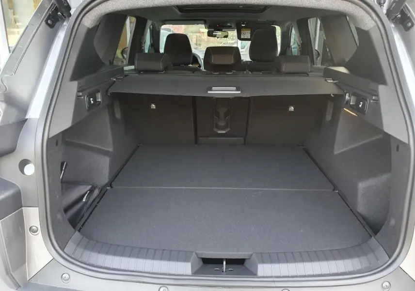 Coffre ouvert vu de l'arrière du Dacia Bigster gris schiste avec cache-bagages et banquette arrière rabattue.