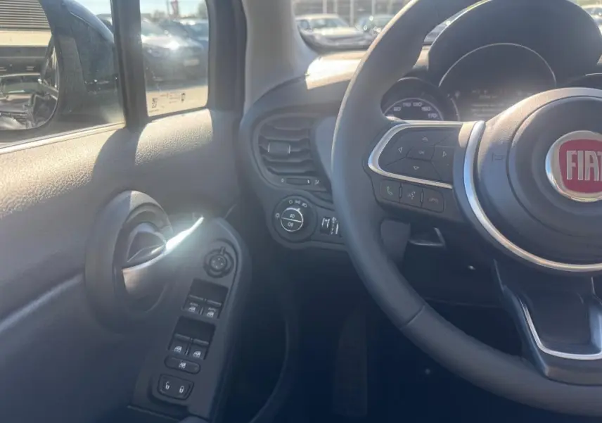 Vue intérieure côté gauche du volant d'une FIAT 500X bleu, avec commandes des vitres et volant multifonction visibles.