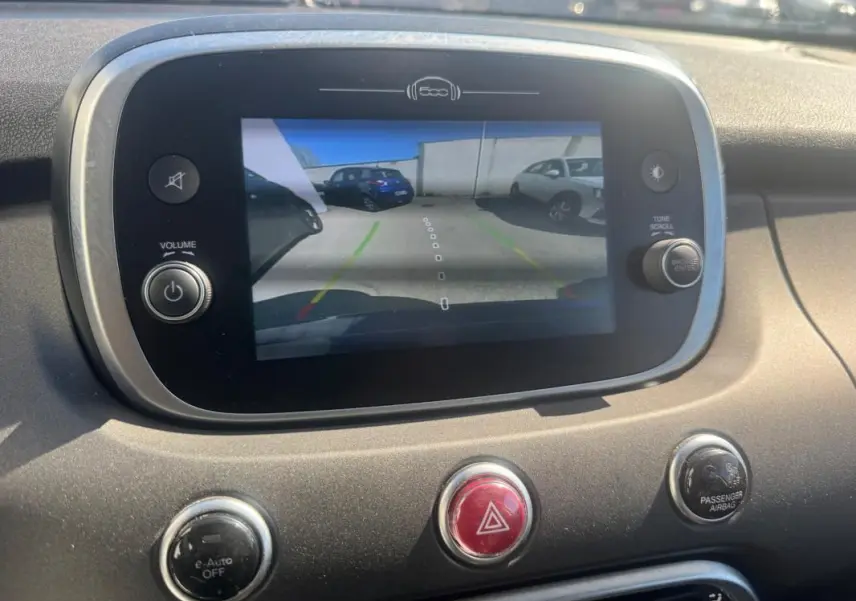 Écran central affichant la caméra de recul d'une FIAT 500X bleu, vue arrière en stationnement extérieur.
