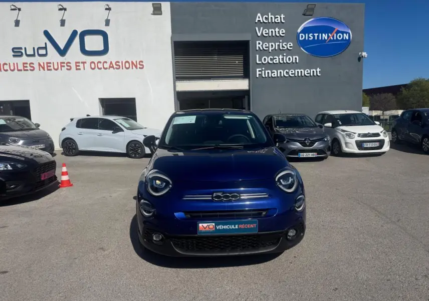 Vue de face d'une FIAT 500X bleu foncé MY23 avec phares ronds et calandre chromée, stationnée en extérieur.