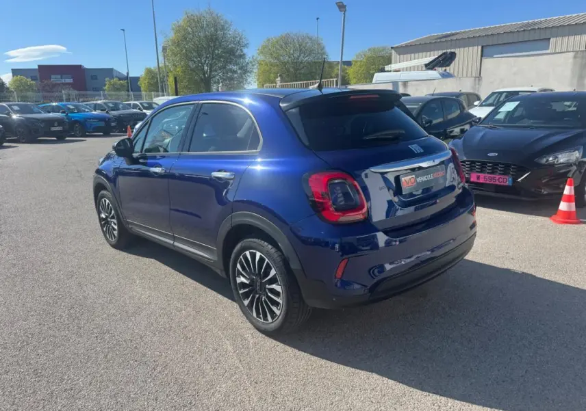 Vue 3/4 arrière droite d'une FIAT 500X bleu métallisé avec jantes classiques 16 pouces, stationnée en extérieur.
