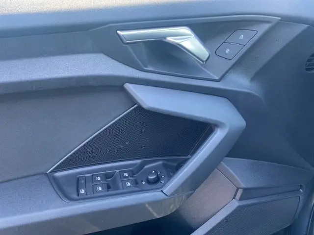 Gros plan sur la porte côté conducteur de l'Audi A3 Sportback gris Manhattan, montrant les commandes des vitres et la poignée intérieure.