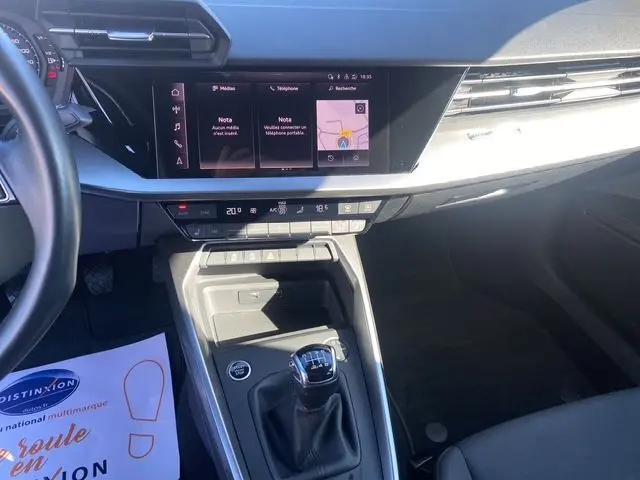 Vue intérieure du tableau de bord et console centrale d'une Audi A3 Sportback gris Manhattan, avec écran tactile et levier de vitesse manuel.
