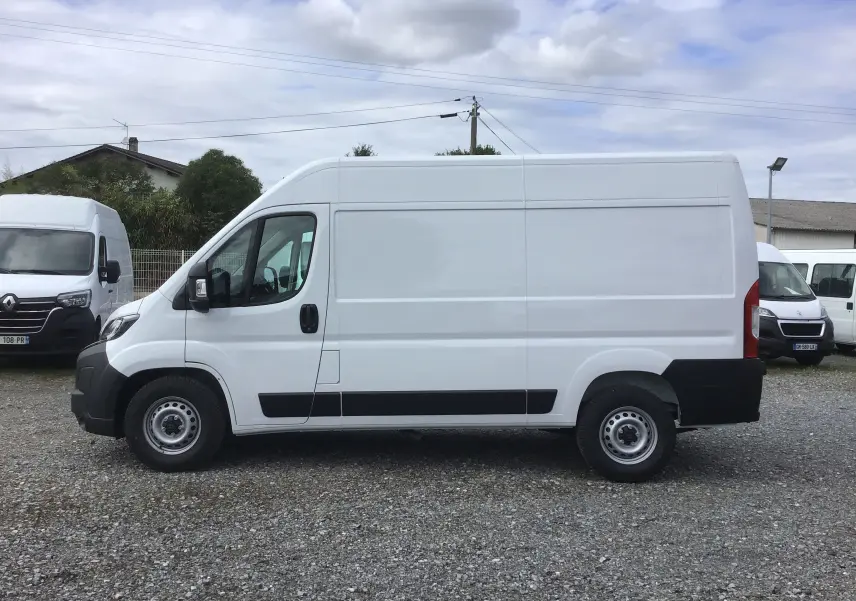 Vue profil côté gauche d'un utilitaire blanc Peugeot Boxer Fourgon L2H2 avec protections noires sur un parking extérieur.