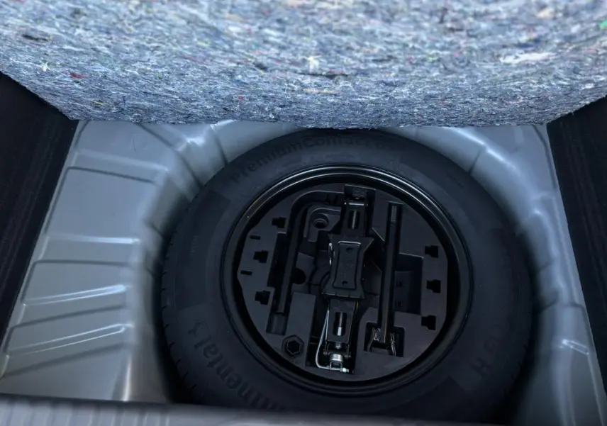 Vue en plongée sur la roue de secours tôle noire et ses outils dans le coffre d'une Renault Clio Gris Schiste 2025.