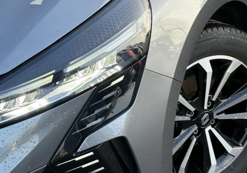 Gros plan sur le phare avant gauche et la jante alliage diamantée noire et argentée d'une Renault Clio Gris Schiste.