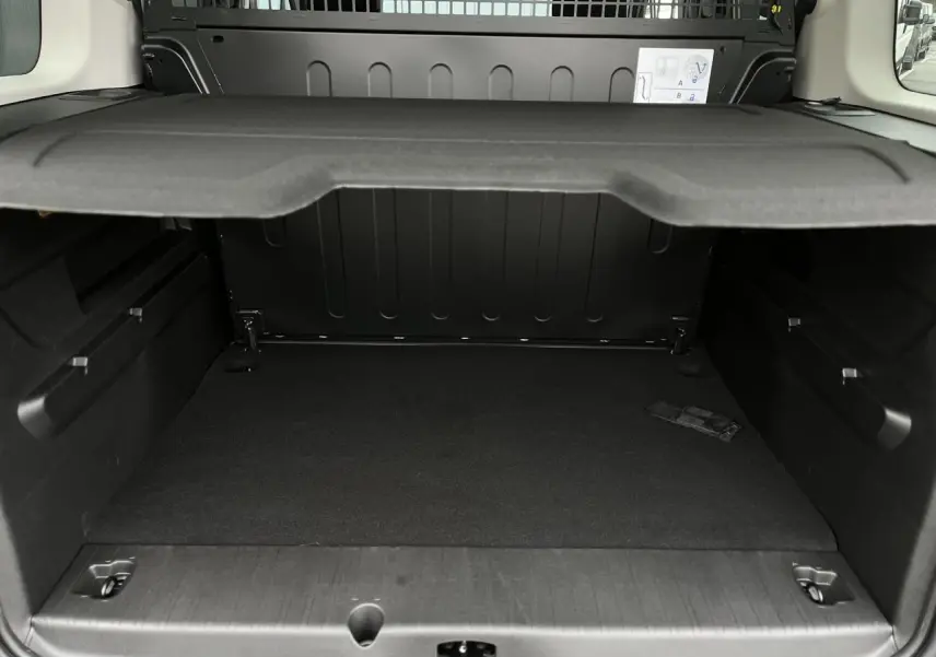 Vue intérieure du coffre noir du Citroën Berlingo Multispace blanc, montrant la tablette cache-bagages relevée.