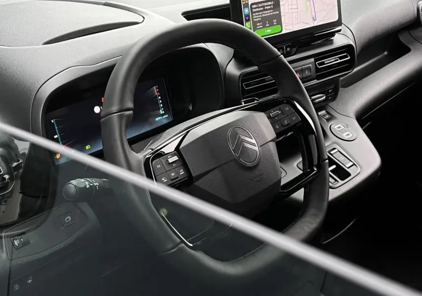 Vue intérieure du poste de conduite du Citroën Berlingo Multispace 2025, volant cuir multifonctions et écran tactile visible.