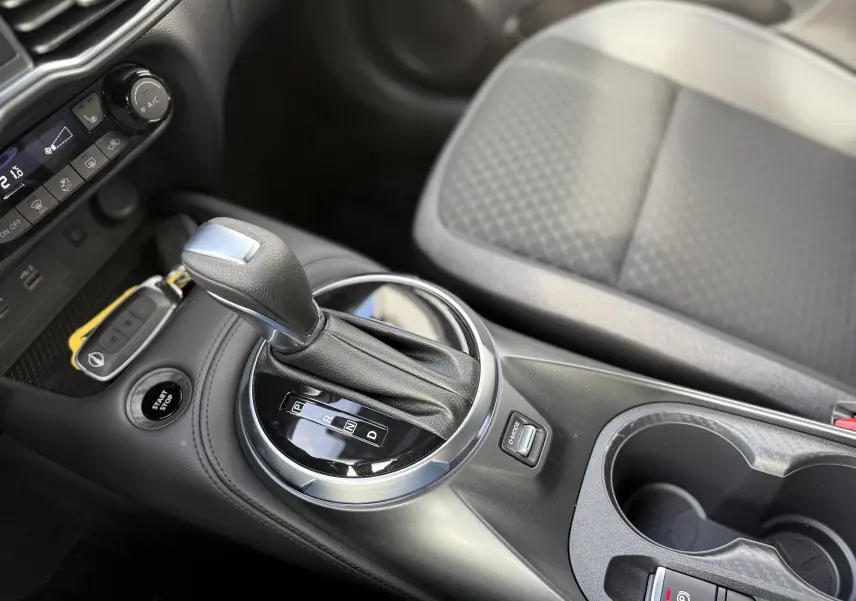 Gros plan sur la console centrale du Nissan Juke 2025, montrant le levier de vitesse automatique et les commandes environnantes.