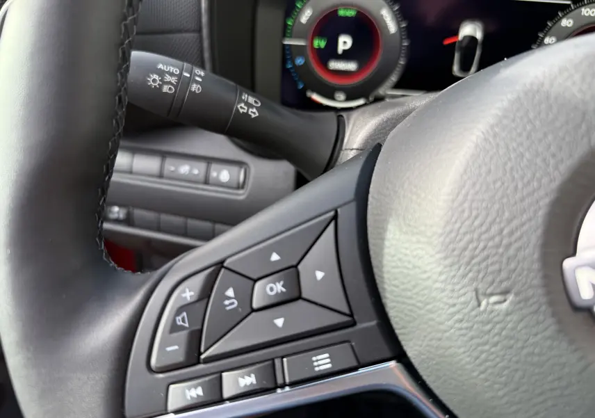 Gros plan sur le volant côté gauche du Nissan Juke rouge Fuji 2025, avec commandes multifonctions et tableau de bord numérique.