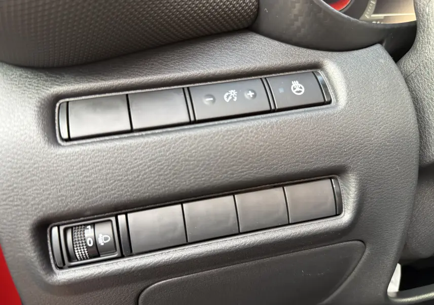 Gros plan sur les commandes de réglage d’éclairage et de volant chauffant dans un Nissan Juke rouge Fuji, côté conducteur.